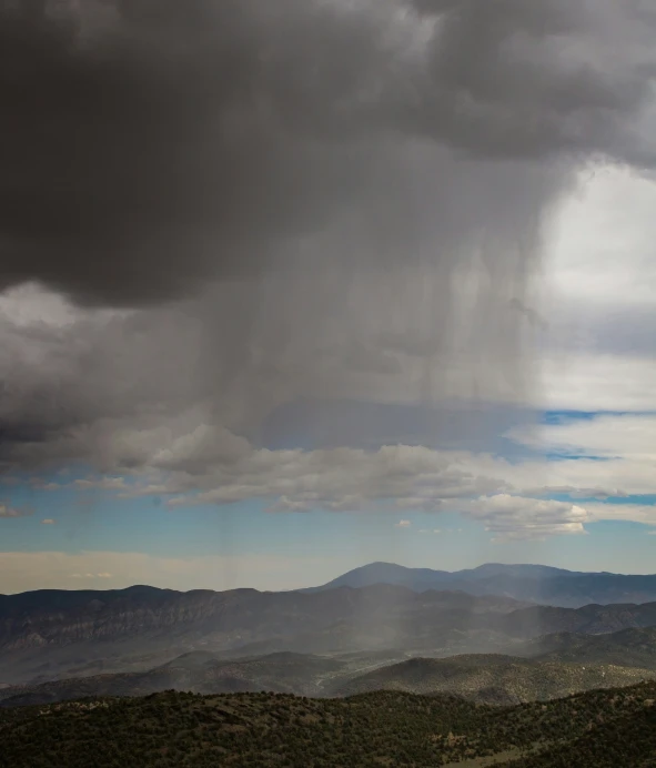 an overcast, rainy landscape with mountain ranges in the distance