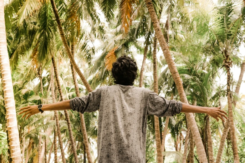 a man with his arms open stands among palm trees