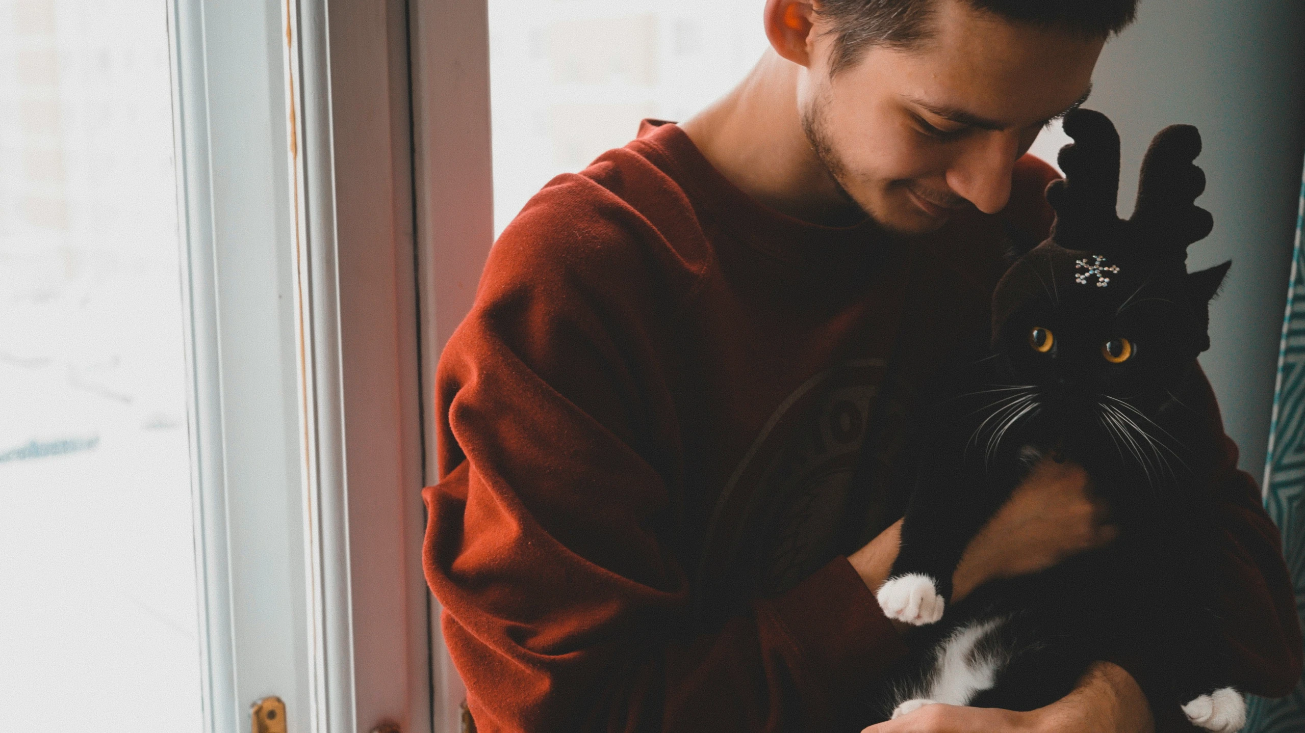 man holding a black and white cat near the window