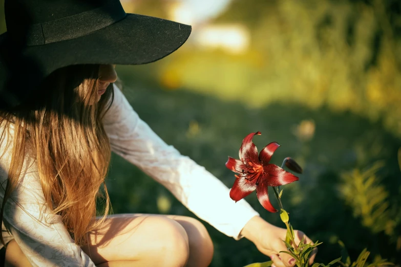 woman in black hat kneeling down holding up a red flower