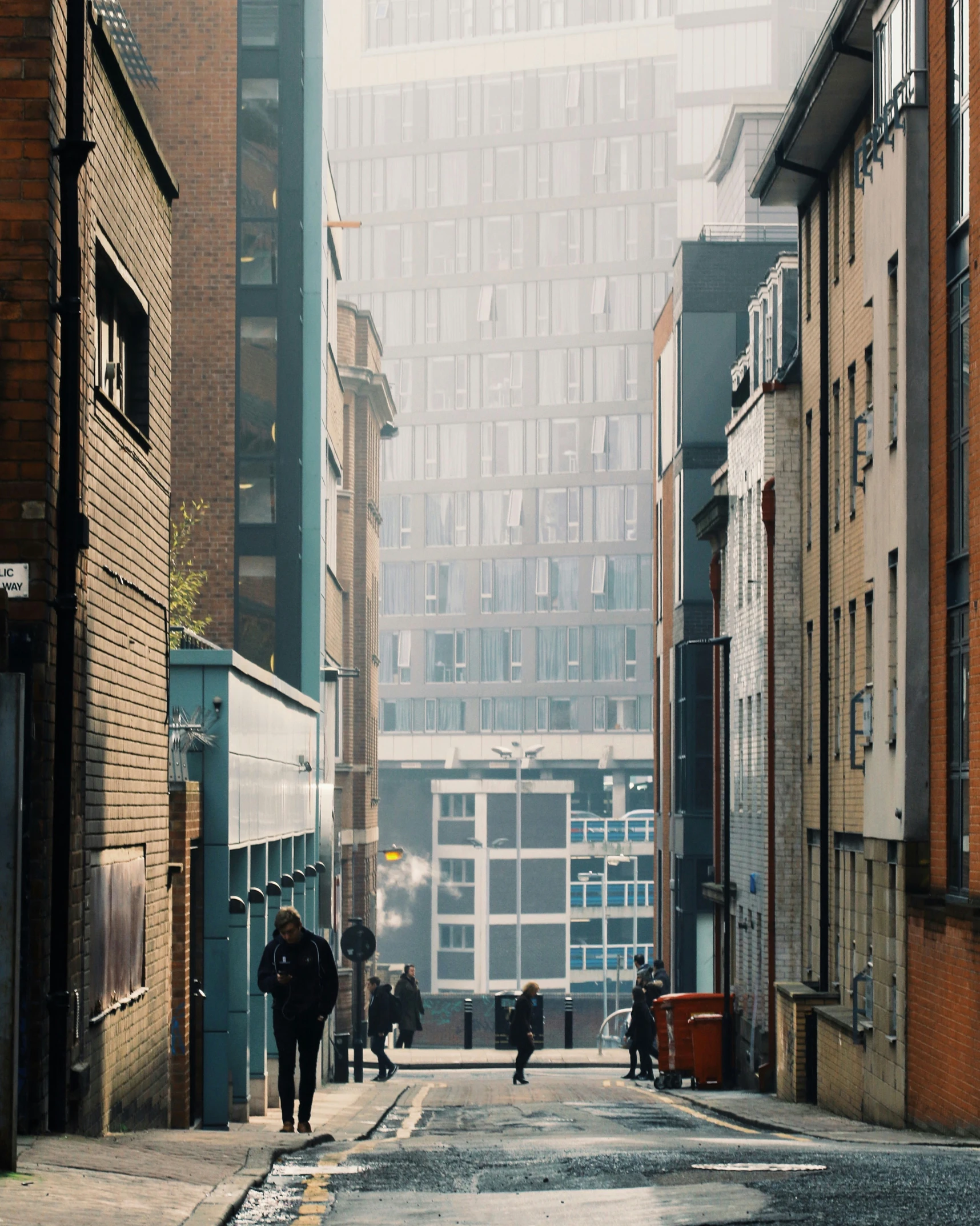 a city alley with people walking and a few cars