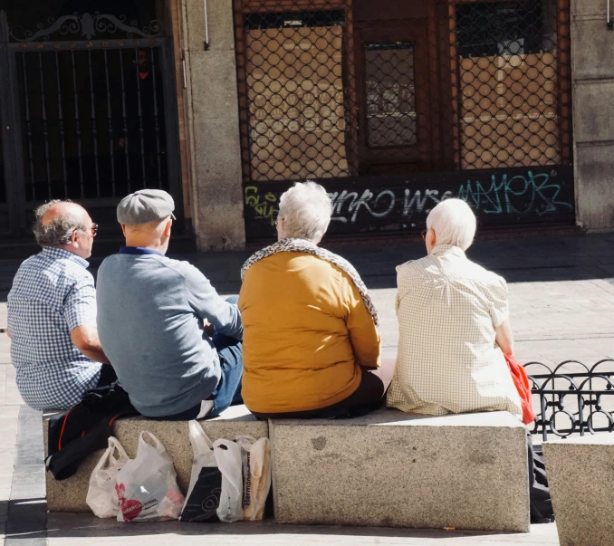 four people sitting on a bench looking at a building with graffiti