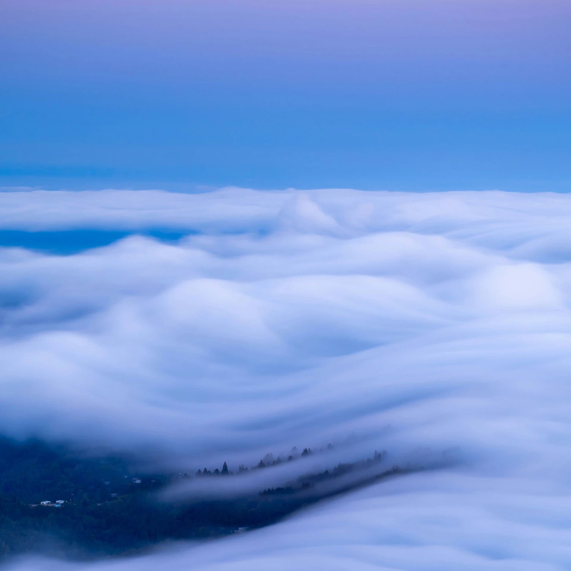 a cloud bank flying over mountains under blue sky