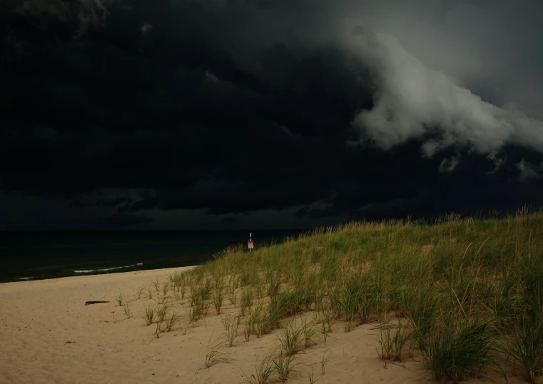 a large storm looms over a sand dune next to the ocean