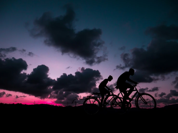 two people riding bicycles in front of a dark sky