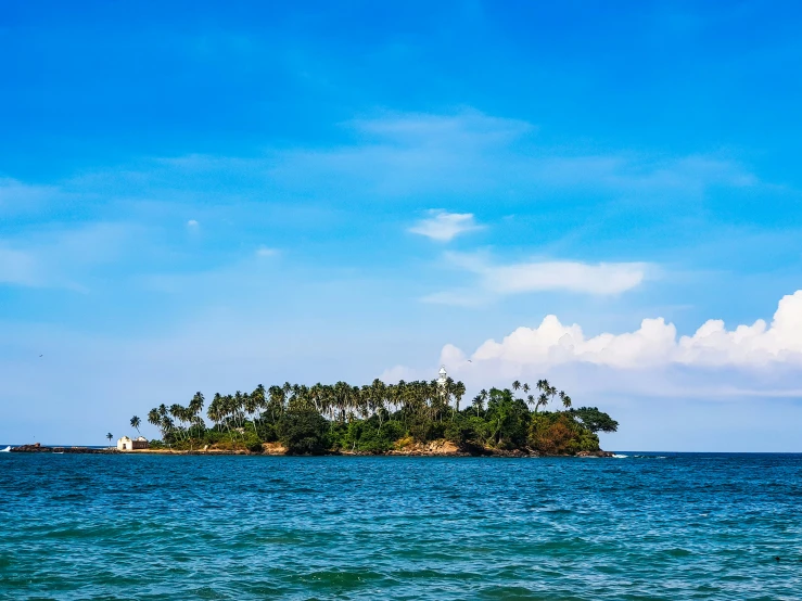 a small island sits in the middle of an ocean with lots of palm trees on one end and blue sky with a few clouds