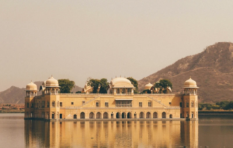 an old building near water with mountains in the background