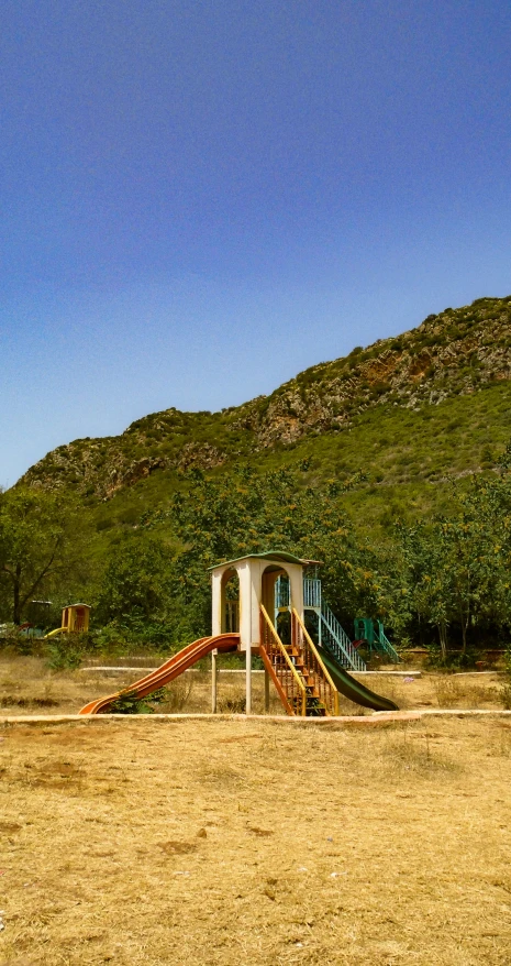 the playground with slides, trees and bushes on the hill