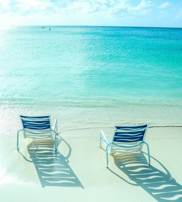 two beach chairs sit on the sand with their shadows projected by water