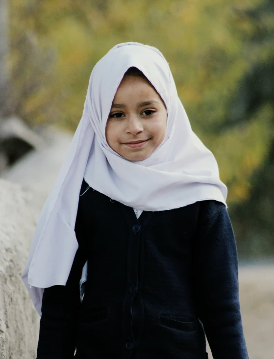 a child in a white headscarf standing by a stone wall