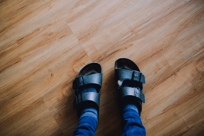 two feet standing on the wooden floor with sandals on