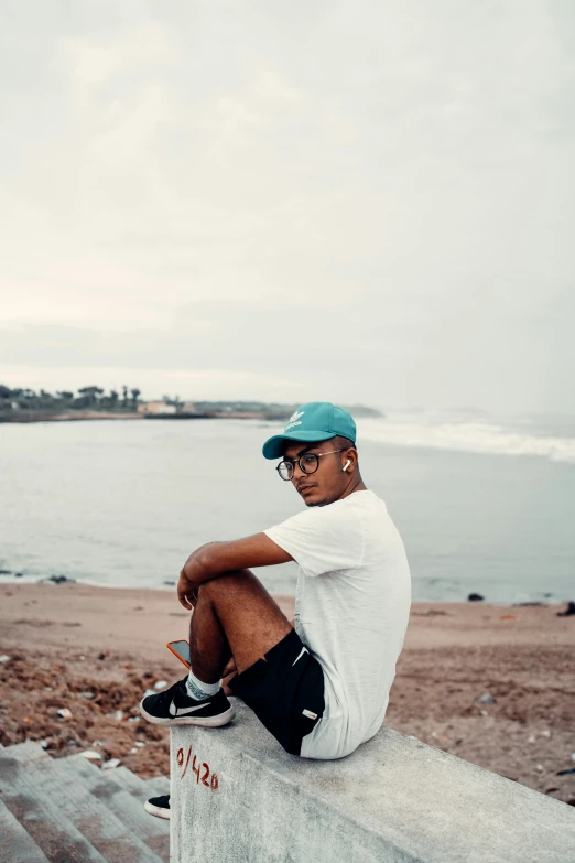 a man with a green cap sitting on a wall overlooking the ocean