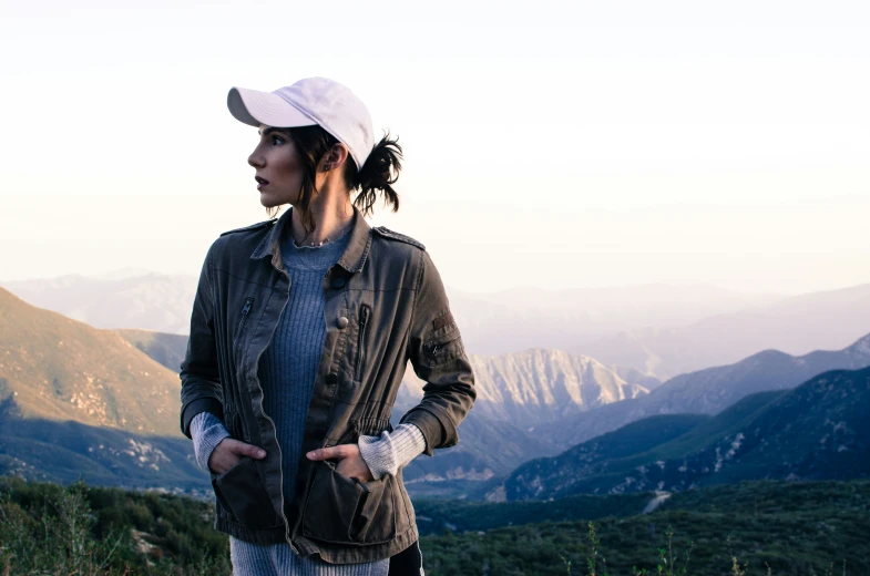 a woman wearing a white hat standing at the top of a mountain