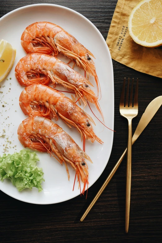 cooked shrimp on a plate with lemon wedges next to a fork and knife