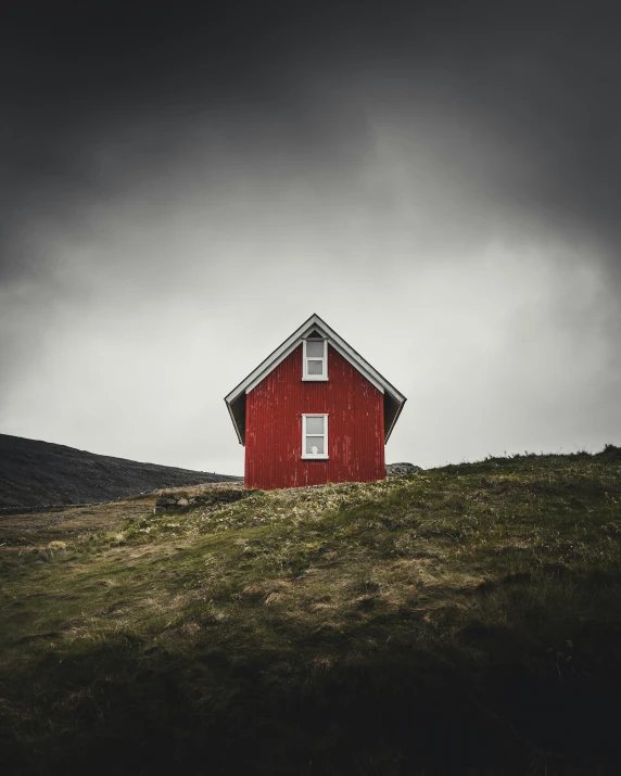 red house with a sloping top on hillside under a stormy sky