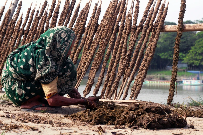 woman with green headscarf sitting on the ground in front of a pile of twigs