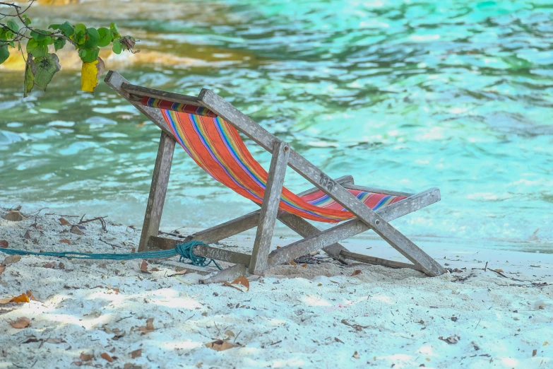 an empty lawn chair sitting on the sand next to a body of water