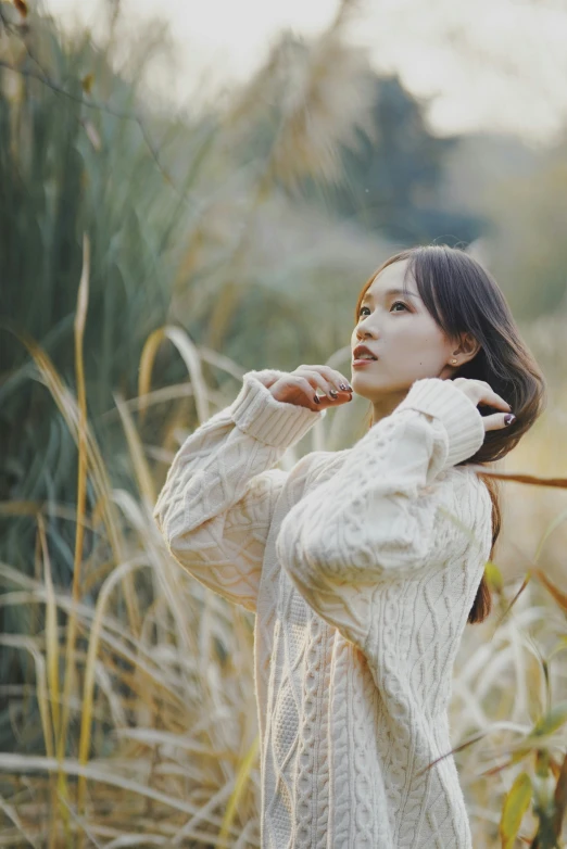 an asian woman stands in tall grass and poses for the camera