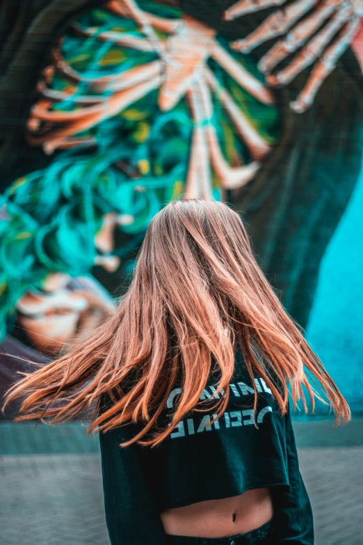 a woman standing near a colorful mural holding onto her hair