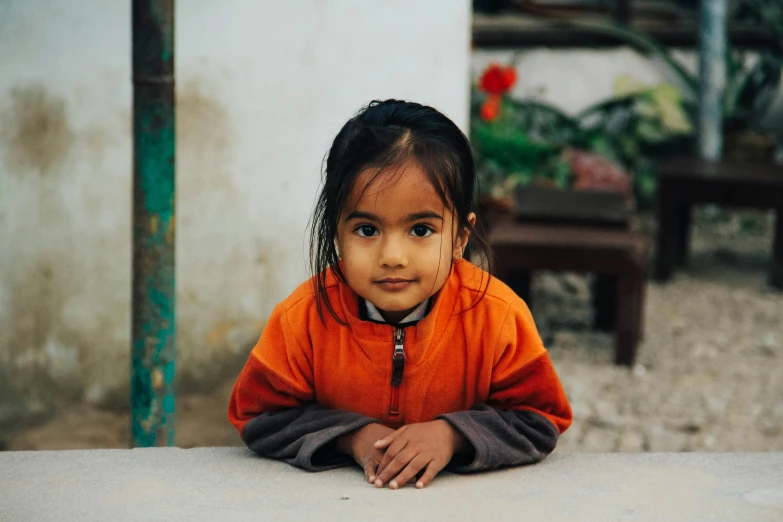 a small child wearing an orange and brown jacket sitting on the ground