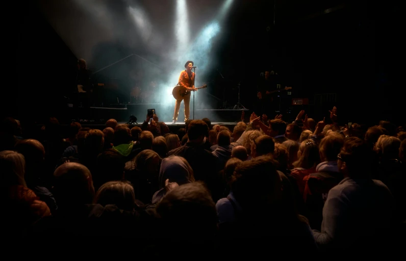 a man standing on stage holding a microphone with audience behind him