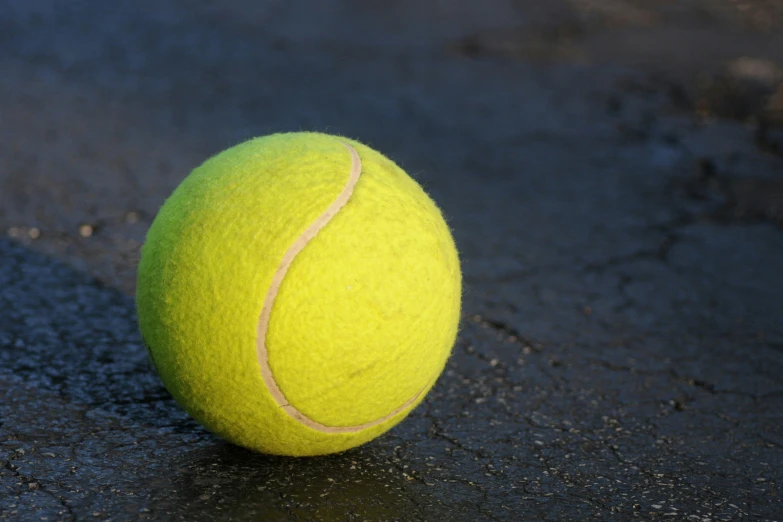 a tennis ball sits on the ground in front of a shadow