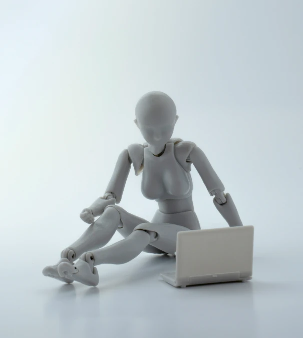 a plastic doll sits on the floor while using a laptop