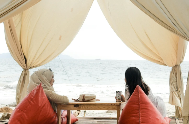 two women are sitting outside having coffee by the beach