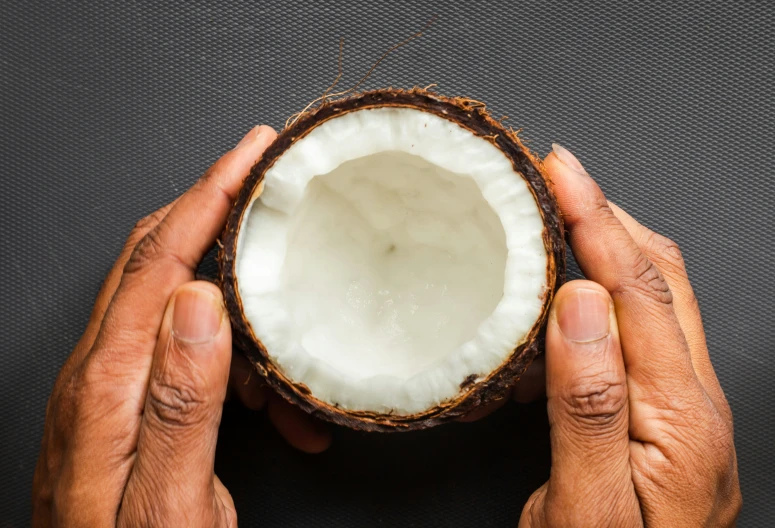 two hands holding up a coconut with some dirt