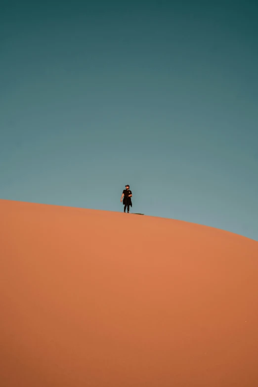 the man is standing on top of the sand dune