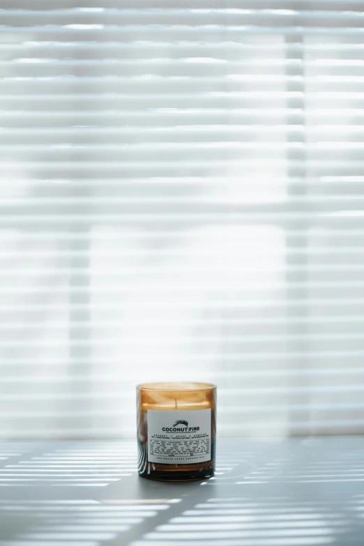 a candle in front of a window with the blinds drawn on it