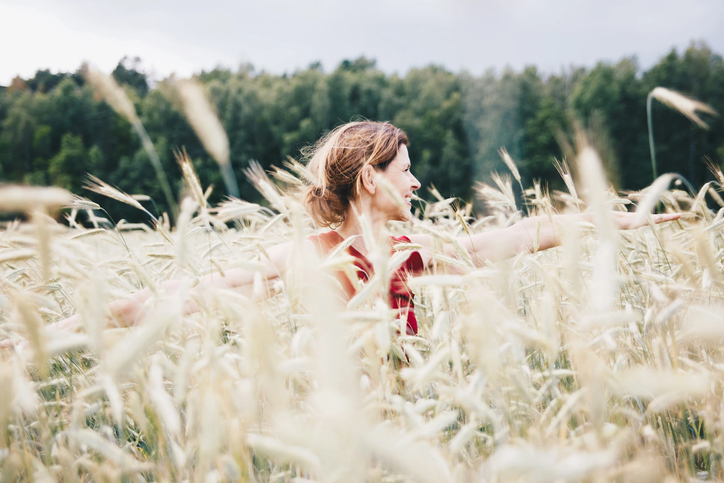 a woman standing in tall grass with trees behind her