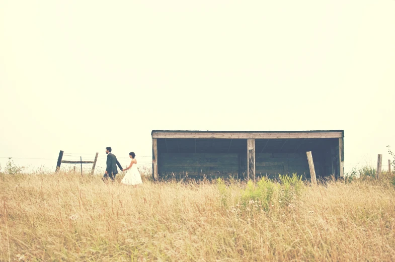 two people walking through tall grass toward an outhouse