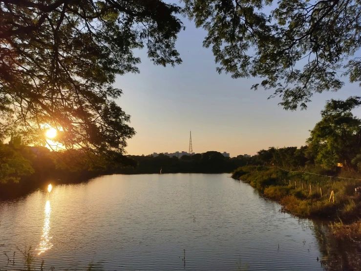 the sun sets over a small lake with an antenna tower in the distance