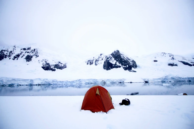 a tent set up in the snow next to a lake