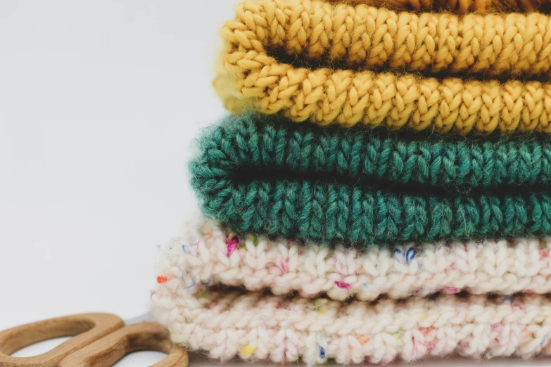 a pile of colored knitted cloths next to a pair of wood handled scissors