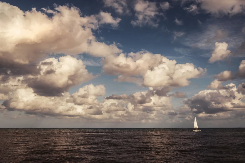 a sailing boat on the ocean with clouds and blue sky