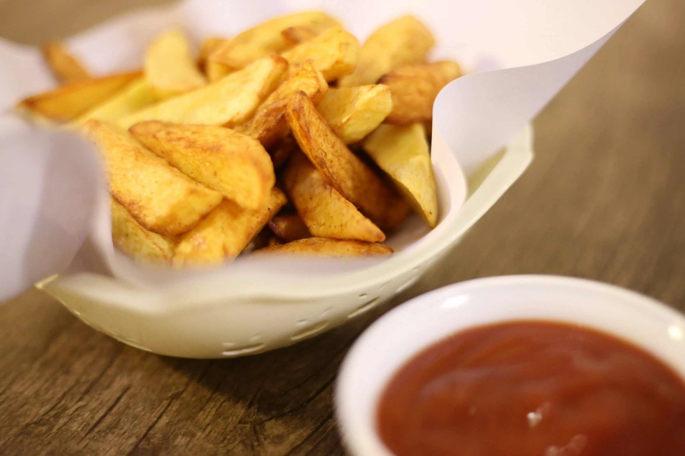 a wooden table holding a basket of french fries and sauce