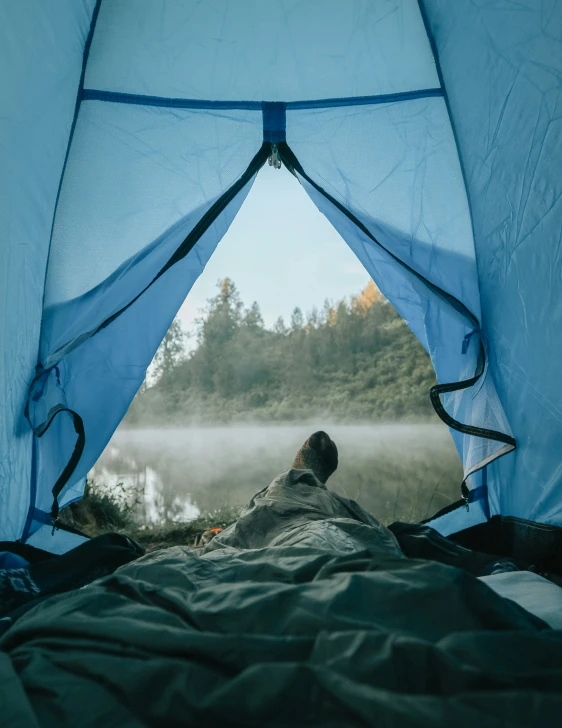 person in tent overlooking water on foggy day