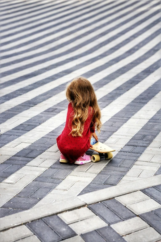 a little girl sitting on the floor near a skateboard