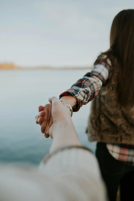 a man and woman holding hands as they walk near the water