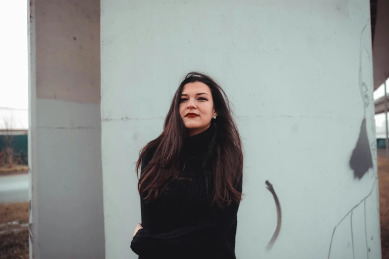 a woman standing outside against the side of a white wall