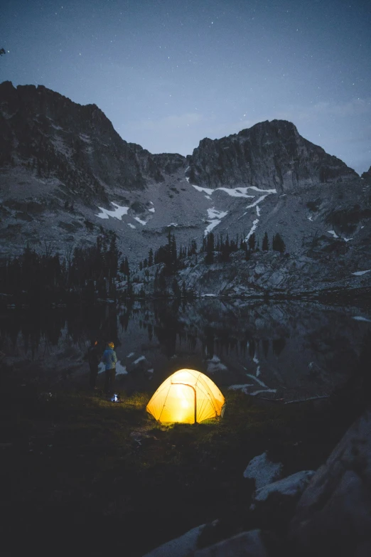 an illuminated camping tent is setting in the mountains