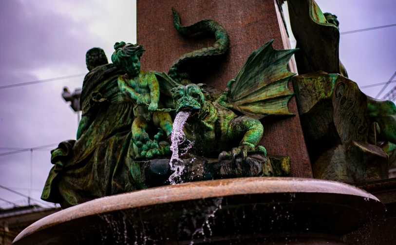 some green statues and a water feature on a pillar