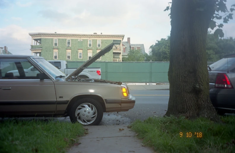 the car has a hood up and is parked next to the tree