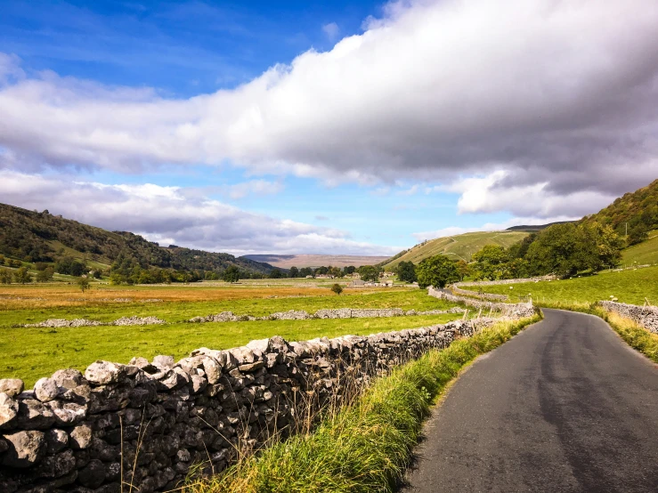 an empty road in the mountains next to a stone wall