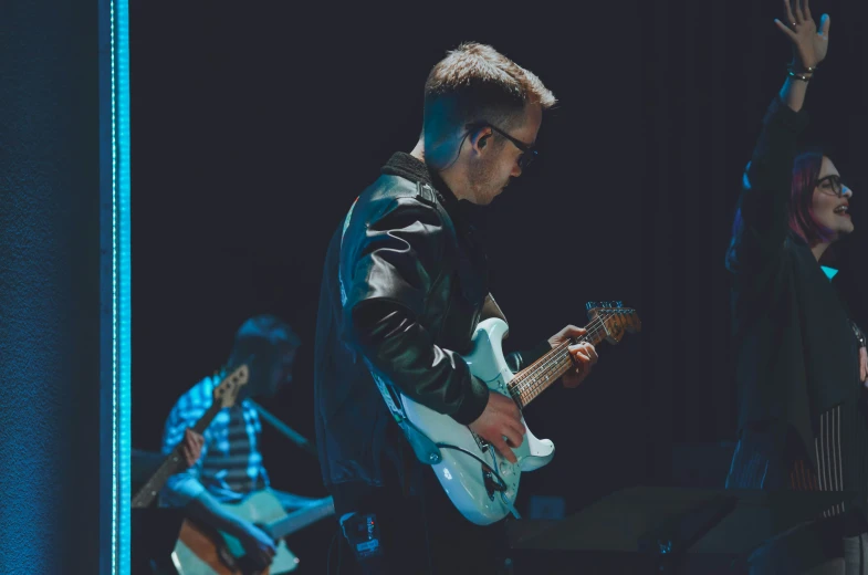 two men and one woman playing a guitar on stage