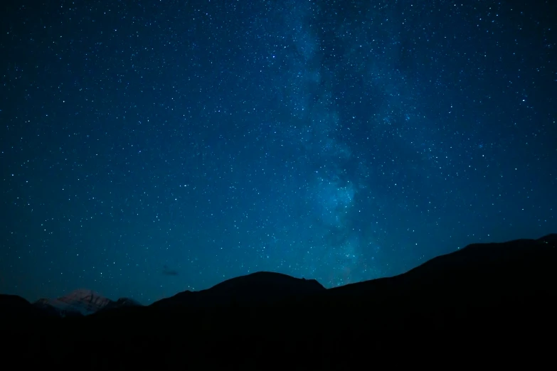 the night sky has stars above a mountain range