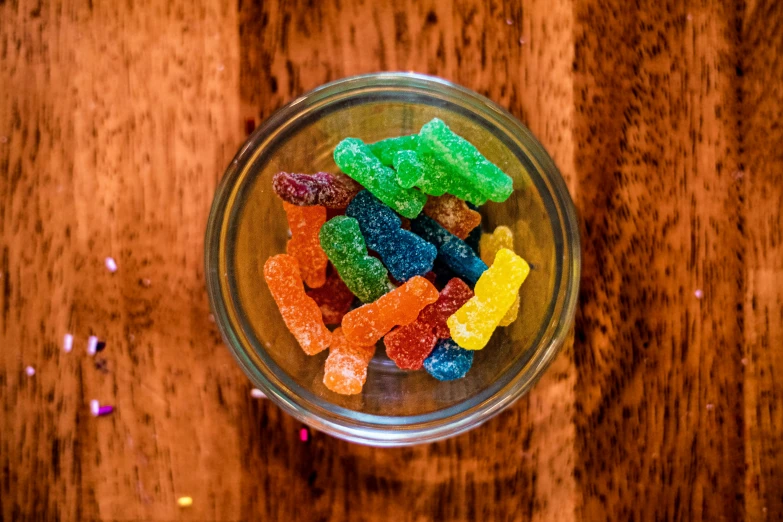 a glass bowl filled with multicolored gummy bears on top of a wooden table