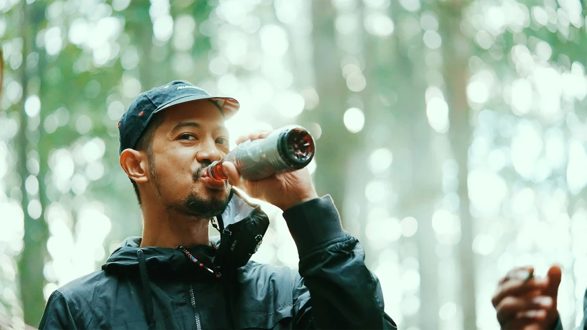 man drinking from silver bottle in the middle of woods